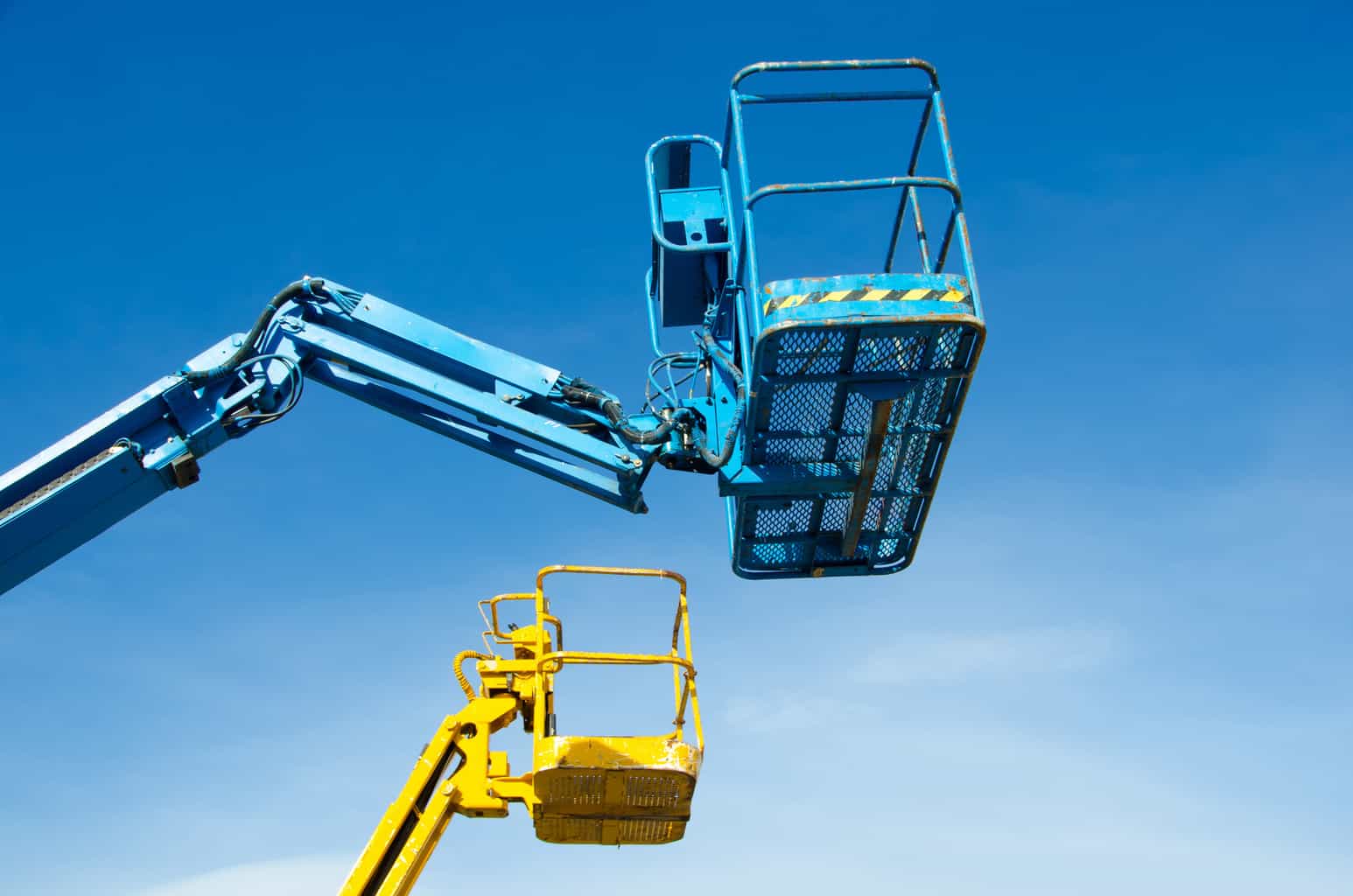 Two crane's baskets against clear sky. Lifters in blue and yellow